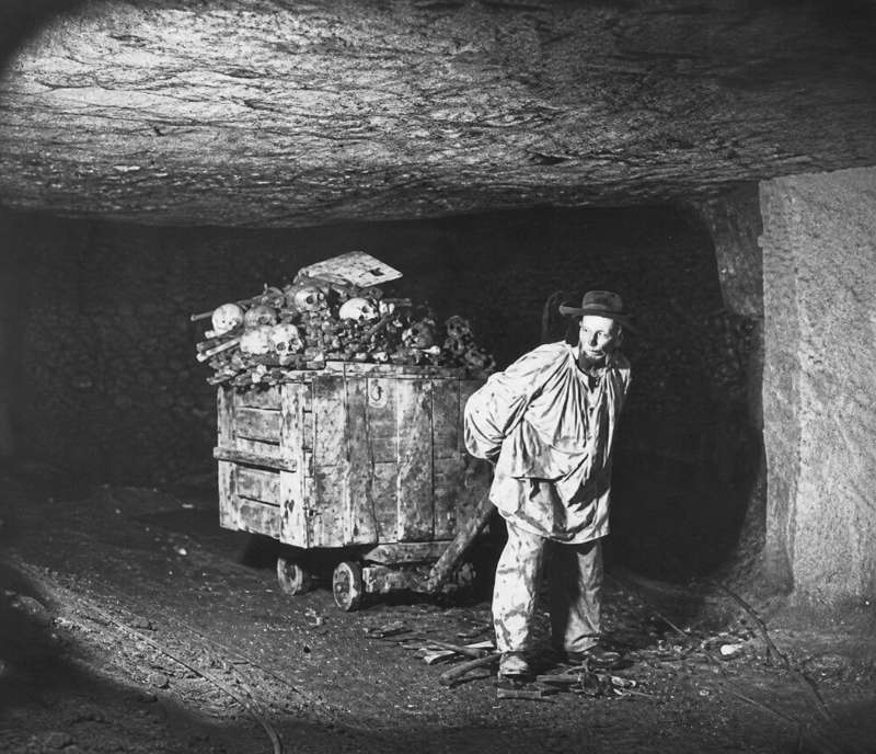 Worker moving bones in the galleries of the Paris Catacombs before their arrangement into decorative hagues.
