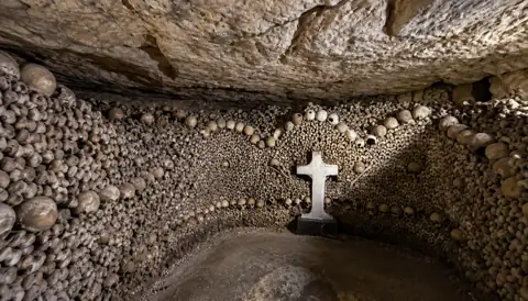 Croix de pierre dans une chambre bordée d’ossements